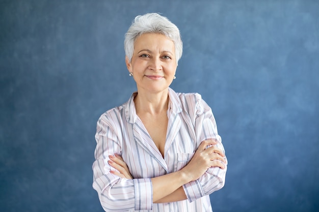 Attractive retired female with short gray hair posing with confident smile crossing arms on her chest