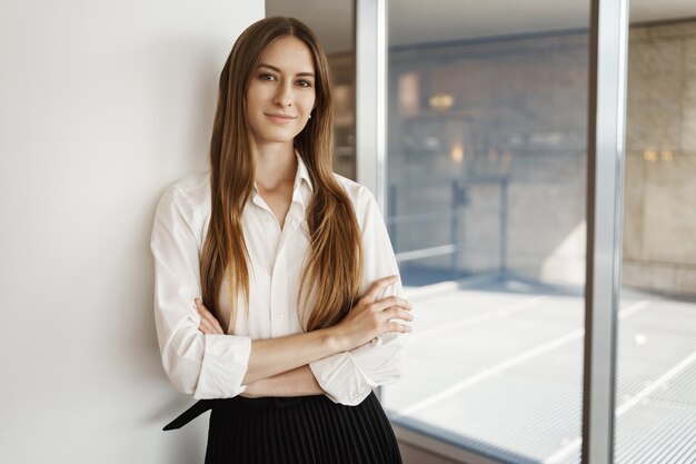 Attractive satisfied young female entrepreneur standing proud, smiling with crossed hands confident