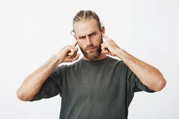 Attractive serious bearded man covering his ears