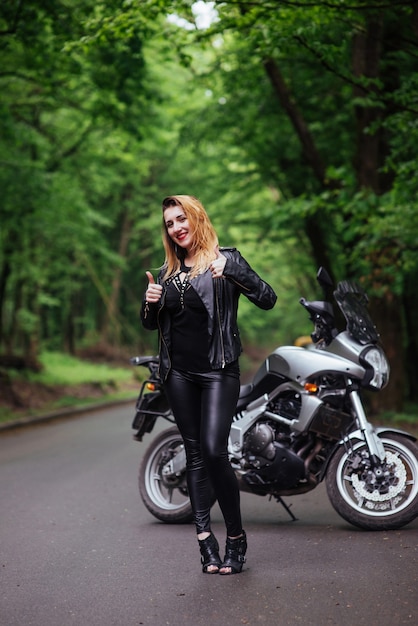 Привлекательная сексуальная девушка, одетая в кожу, позирует возле спортивного мотоцикла на улице