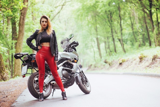 외부 스포츠 오토바이 근처에 포즈를 취하는 빨간 가죽을 입은 매력적인 섹시한 여자