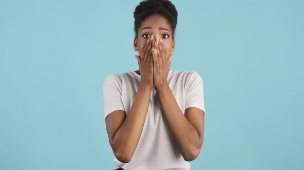 Attractive shocked casual african american girl emotionally covering face with hands on camera over colorful background