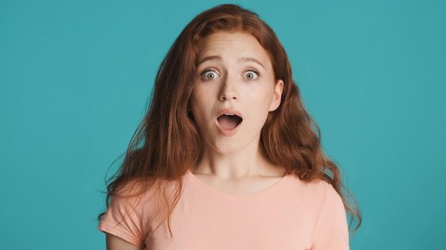 Free photo attractive shocked redhead girl amazedly looking in camera with open mouth over colorful background wow expression