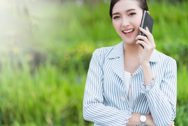 Free photo attractive smile cheerful asian female businesswoman smartphone communication technology building garden outdoor location free copysapce