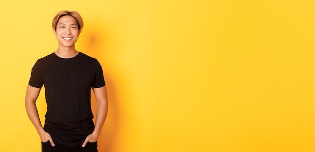 Free photo attractive smiling asian man in black tshirt standing pleased yellow background