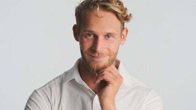 Attractive smiling blond bearded man confidently looking in camera and smiling over white background