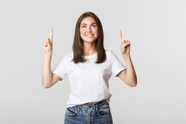 Attraente ragazza bruna sorridente che punta le dita verso l'alto, mostrando il logo.