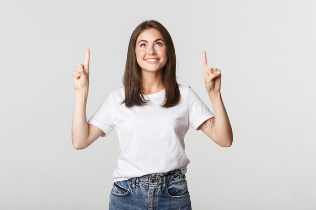 Attractive smiling brunette girl pointing fingers up, showing logo.