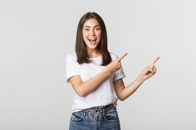 Attractive smiling brunette girl pointing fingers upper left corner, showing logo.