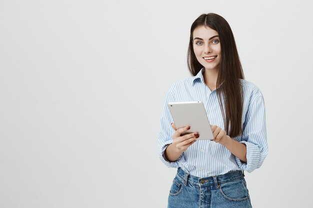 Привлекательная улыбающаяся темноволосая женщина с помощью цифрового планшета