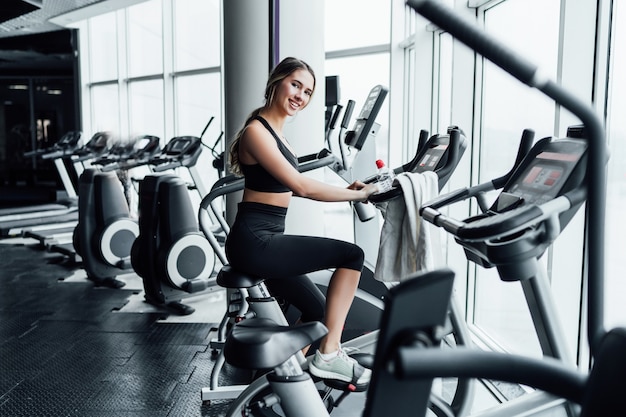 Attractive smiling girl onn exercise bike in a modern spacious gym