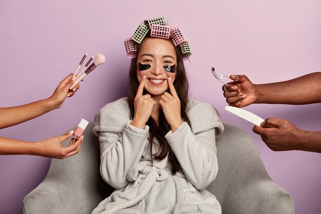 Attractive smiling lady wears black collagen patches under eyes, enjoys beauty treatment