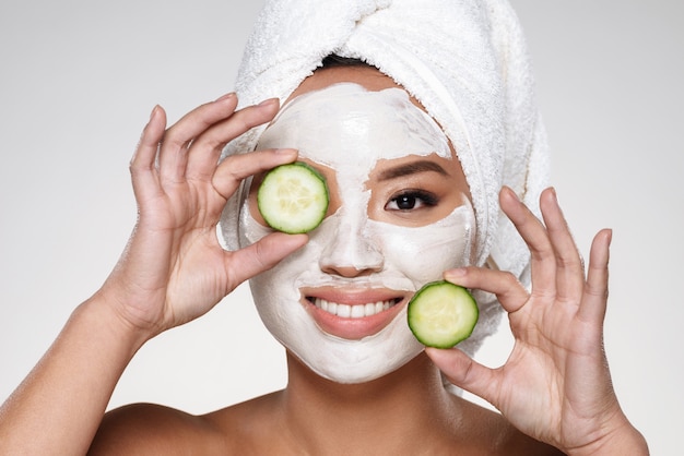 Attractive smiling lady with scrab on face holding cucumber slices