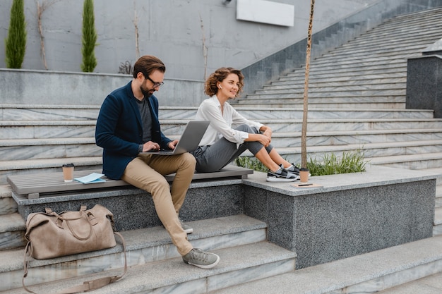 Attractive smiling man and woman sitting on bench in urban city center, making notes