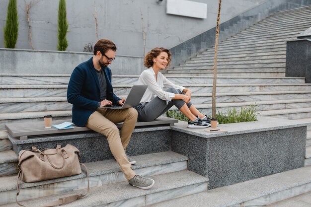 Attractive smiling man and woman sitting on bench in urban city center, making notes