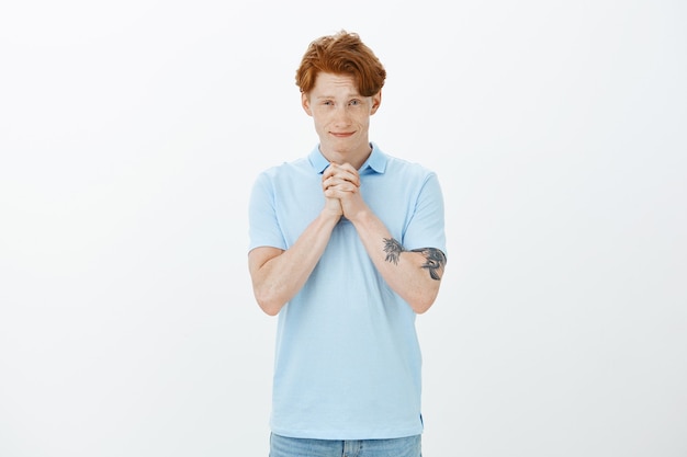 Free photo attractive smiling redhead man clench hands together in plead, begging for help or favour