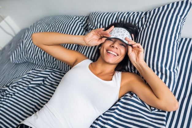 Привлекательная улыбающаяся тощая женщина в пижаме, лежащая в постели дома после отдыха, просыпается утром