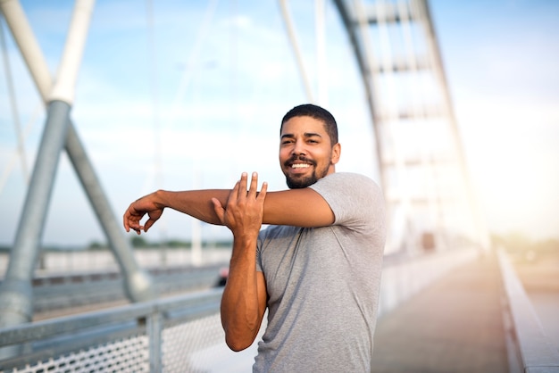 Free photo attractive smiling sportsman warming up his body for an outdoor training