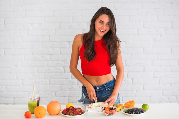 Attractive smiling woman cutting banana on table