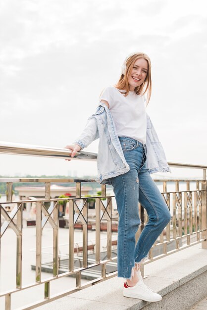 Attractive smiling woman leaning on bridge railing and listening music