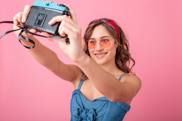 분홍색 배경에 고립 데님 드레스와 선글라스를 착용하는 빈티지 카메라에 자기 초상화 사진을 복용 매력적인 웃는 여자