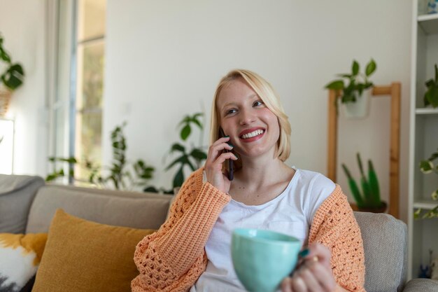 집에서 소파에 앉아 있는 동안 스마트 폰을 사용하는 매력적인 웃는 여성 커뮤니케이션 및 아늑함 개념