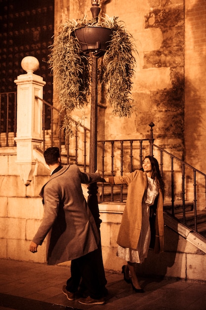 Free photo attractive smiling woman and young man whirling around street lamp