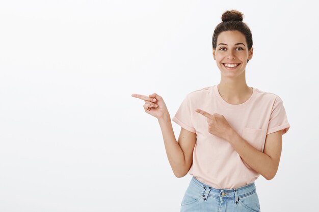 白い壁にポーズをとっている魅力的な笑顔の若いスタイリッシュな女性