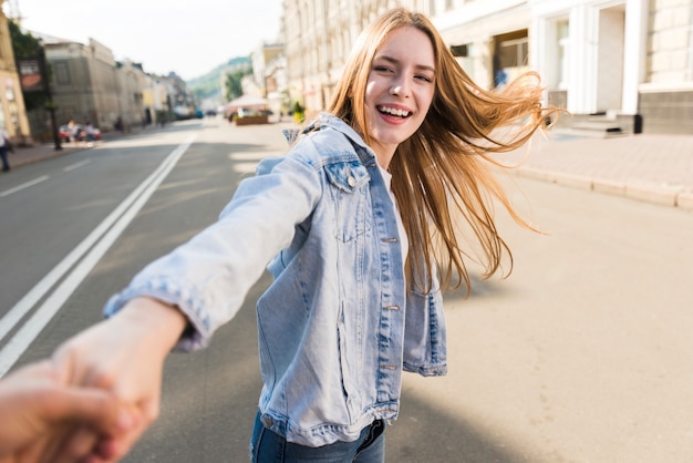 Foto gratuita attraente giovane donna sorridente che porta la mano del suo ragazzo sulla strada