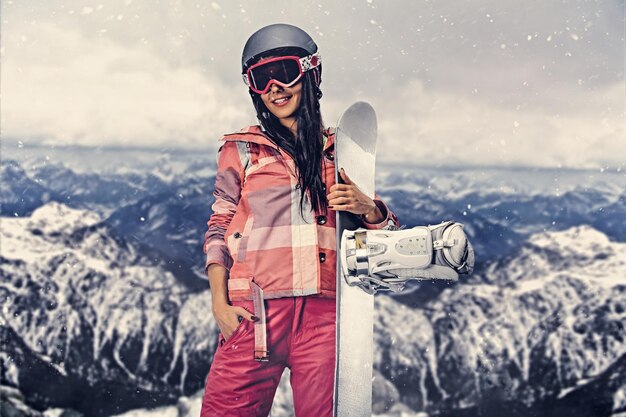 매력적인 스포티 여성은 높은 산에서 사진 세션에서 스노우보드를 보유하고 있습니다.