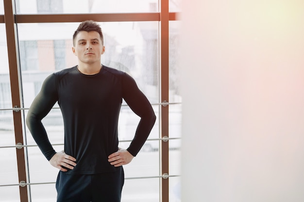 Attractive sporty guy by the window. athlete posing near spacious windows. gym and sports.