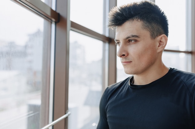 Attractive sporty guy by the window. athlete posing near spacious windows. gym and sports.