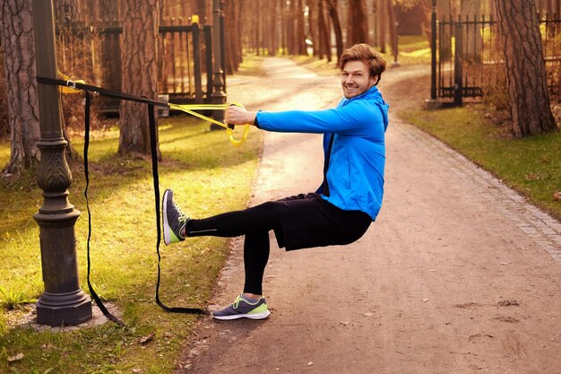 Attractive sporty male exercising with fitness trx strips in a park.