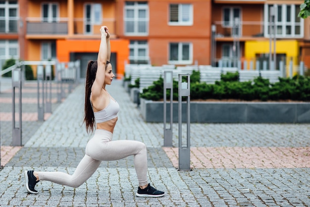 家の近くの街で魅力的なスポーティな女性。スクワットをしている若い完璧な形のブルネット。