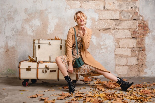거리에서 벽에 가방에 앉아 베이지 색 코트에 매력적인 세련된 금발의 여자