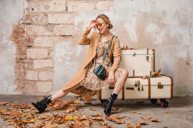 Attractive stylish blonde woman in beige coat walking in street against vintage wall