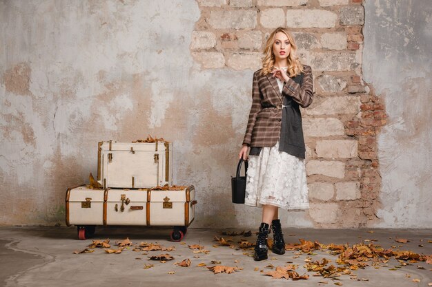 Attractive stylish blonde woman in checkered jacket walking against wall in street