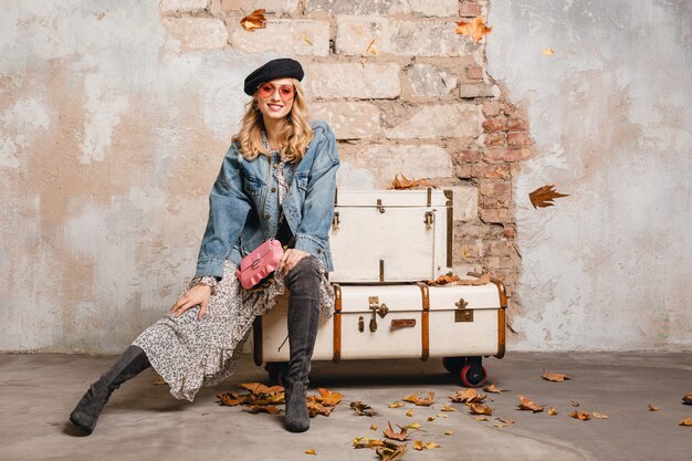 Attractive stylish blonde woman in jeans and oversize jacket walking against wall in street