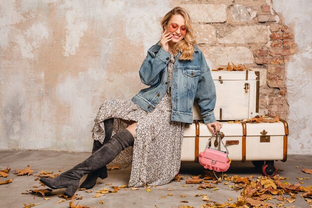 Attractive stylish blonde woman in jeans and oversize jacket walking against wall in street