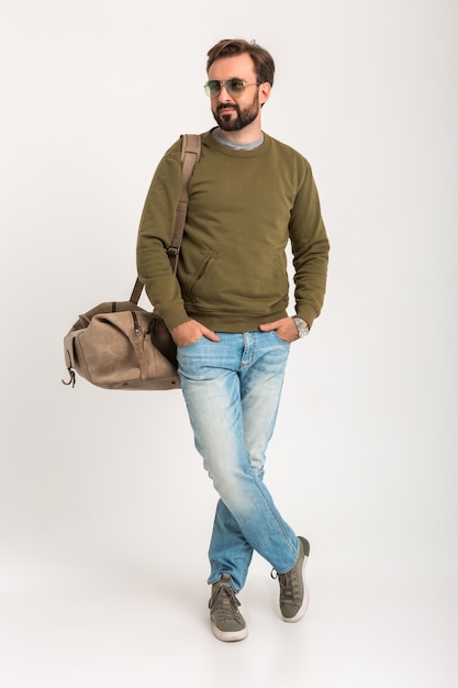 매력적인 세련된 남자 여행자는 청바지와 땀을 흘리는 옷을 입고 잘 생긴 가방으로 서 고립
