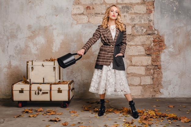 Attractive stylish smiling blonde woman in checkered jacket walking against wall in street