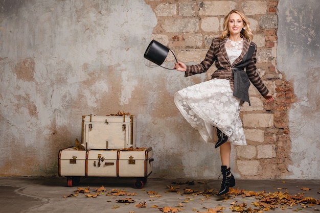 Attractive stylish smiling blonde woman in checkered jacket walking against wall in street