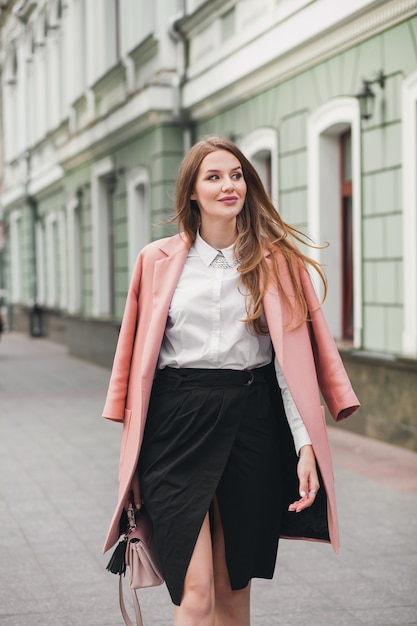 Attraente donna sorridente elegante che cammina per la strada della città in tendenza moda primavera cappotto rosa, stile elegante