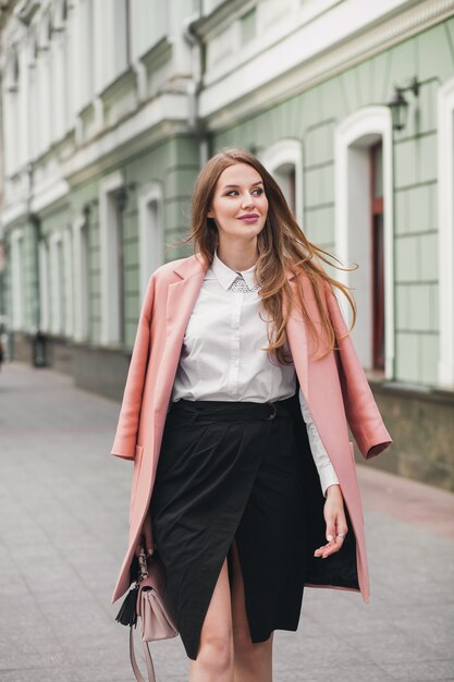 Привлекательная стильная улыбающаяся женщина гуляет по городской улице в розовом пальто весенней модной тенденции, элегантном стиле