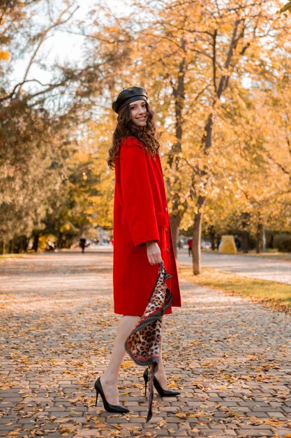 따뜻한 빨간 코트 가을 유행 패션, 스트리트 스타일을 입고 공원에서 산책하는 곱슬 머리를 가진 매력적인 세련된 웃는 여자, 베레모 모자와 표범 인쇄 스카프를 착용