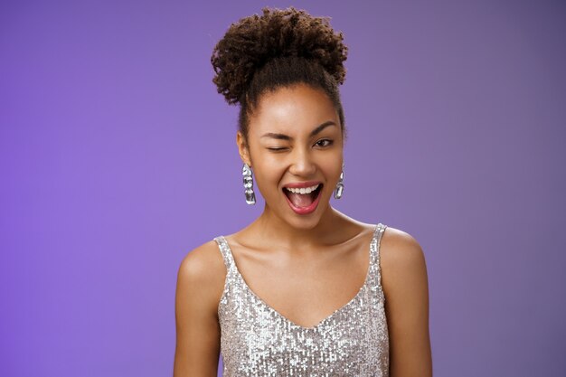 Attractive stylish wealthy african american woman in luxurious earrings silver dress winking asssuring everything ok guarantee your secret safe smiling devious have excellent plan, blue background.