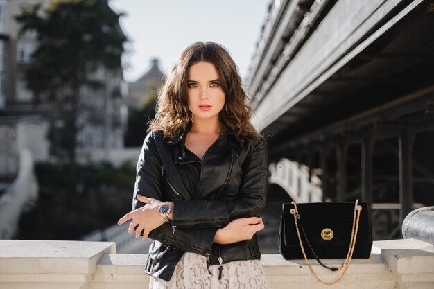 attractive stylish woman posing in street in fashionable outfit, suede handbag, wearing black leather jacket and white lace dress, spring autumn style
