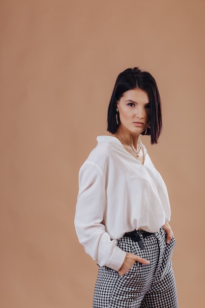 Attractive stylish young girl in business attire posing on cream wall. concept of stylish clothes and sophistication.