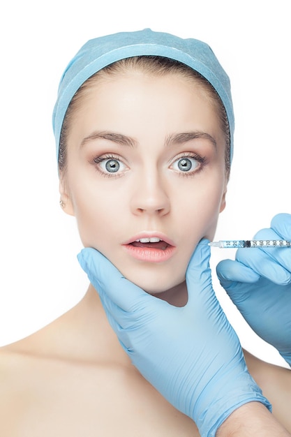 Привлекательная удивленная и испуганная женщина в пластической хирургии со шприцем в лице на белом фоне