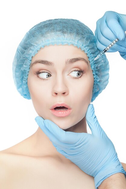 Attractive surprised and scared woman at plastic surgery with syringe in her face on white background